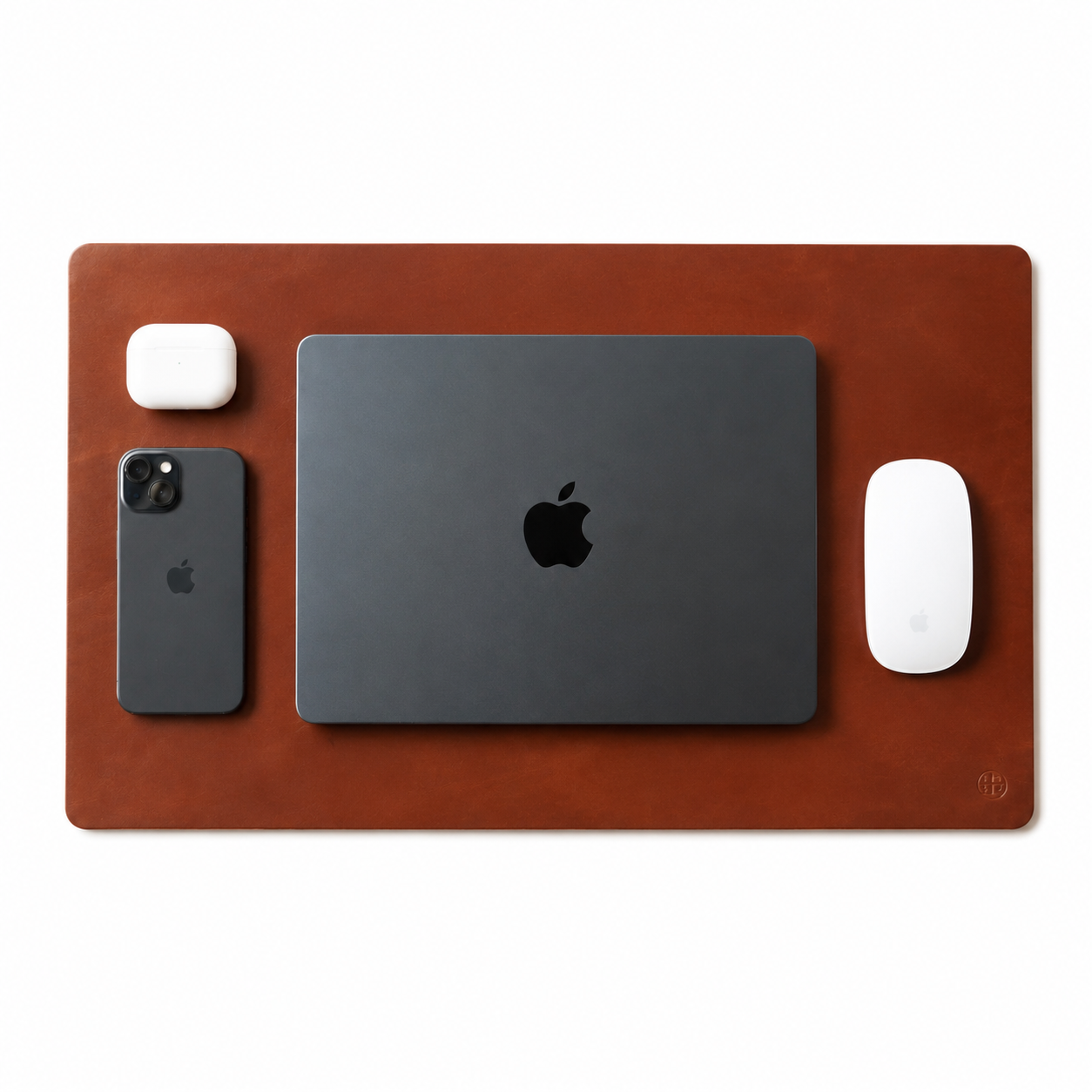 A brown leather desk mat with a small embossed logo in the bottom right corner, styled with a black laptop, a black smartphone, a white earbud case, and a white wireless mouse on a white background.