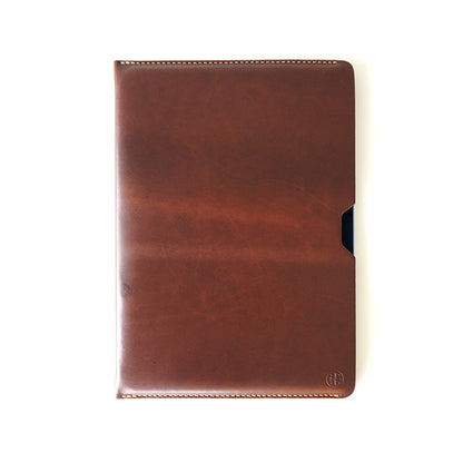 A brown leather folio cover or tablet sleeve with rounded corners, visible stitching, and a small dark side tab, shown on a plain white background.